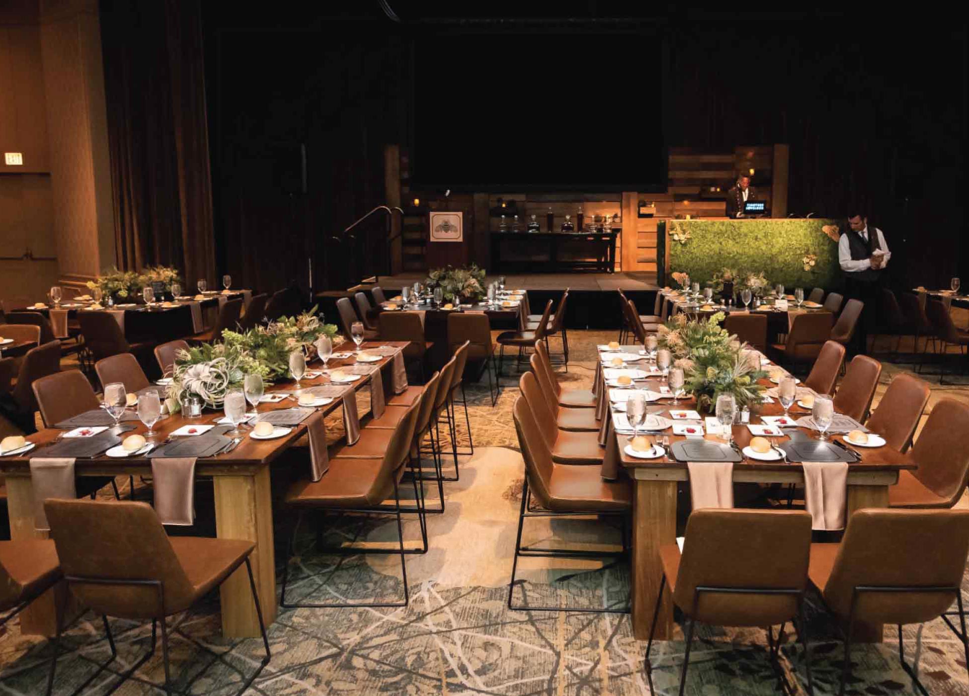 large corporate dinner party with brown chairs and formal-dinning set in dim lit ballroom with food servers