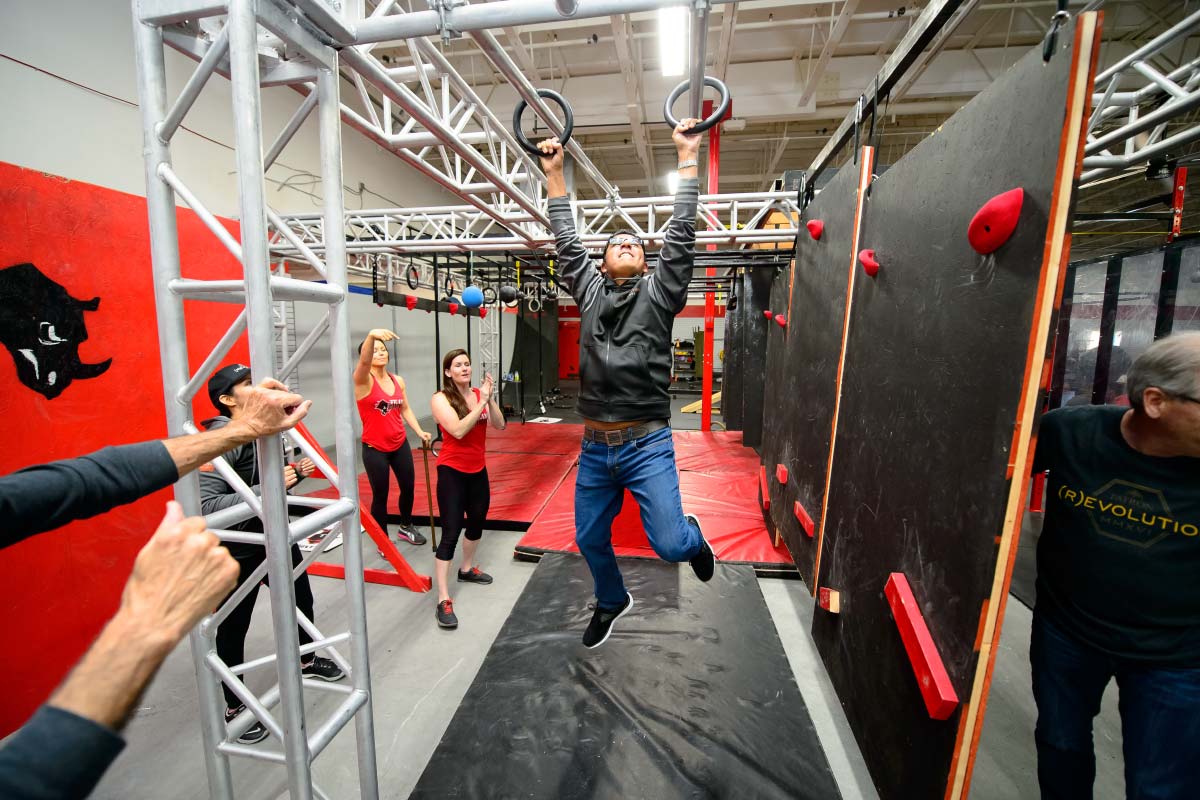 man hanging on gymnastic rings at an indoor obstacle course with rock climbing walls