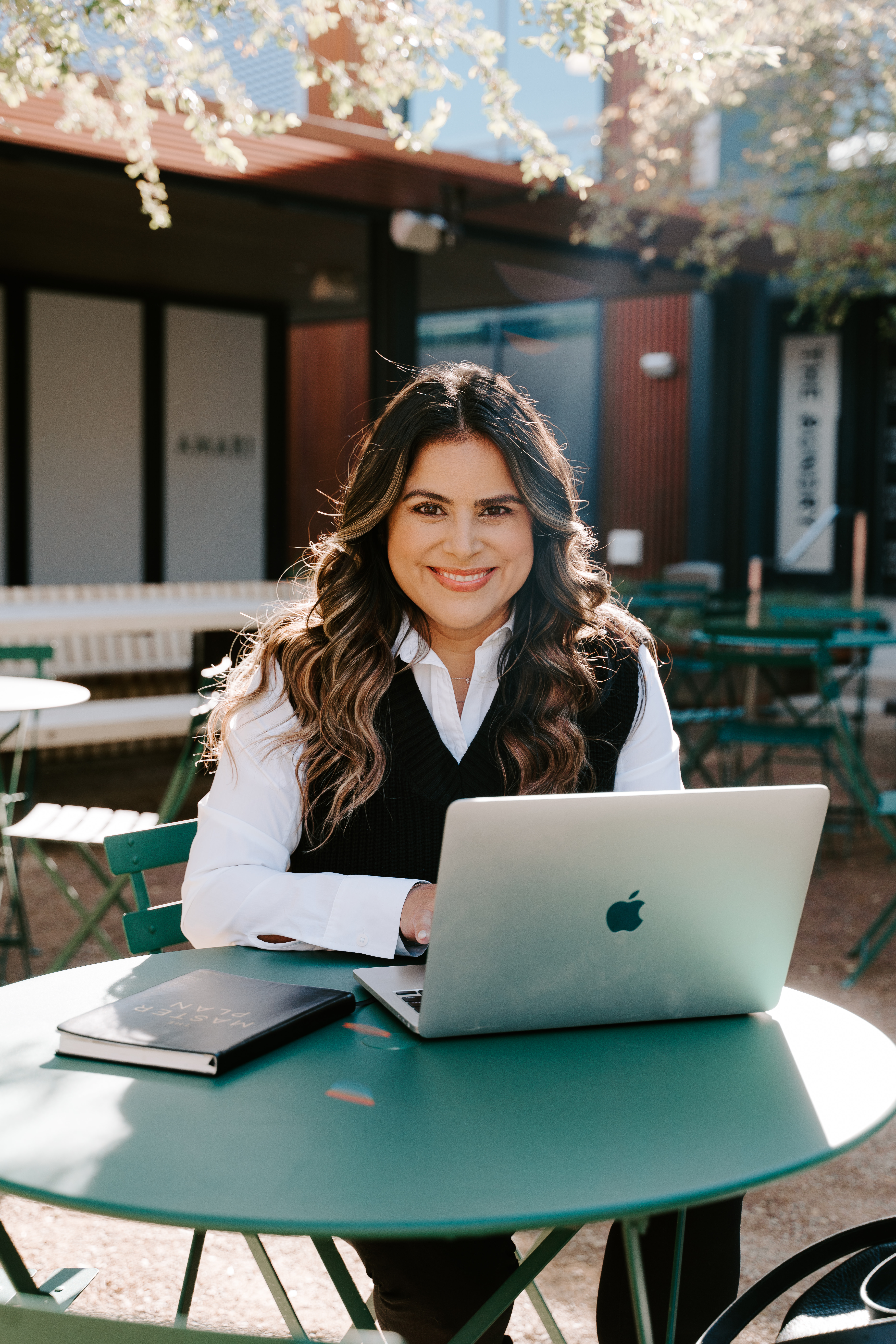 Event Planner CEO and founder or SR Innovations Stephanie Rivera sitting outside in the quad on a green table smiling on her apple laptop